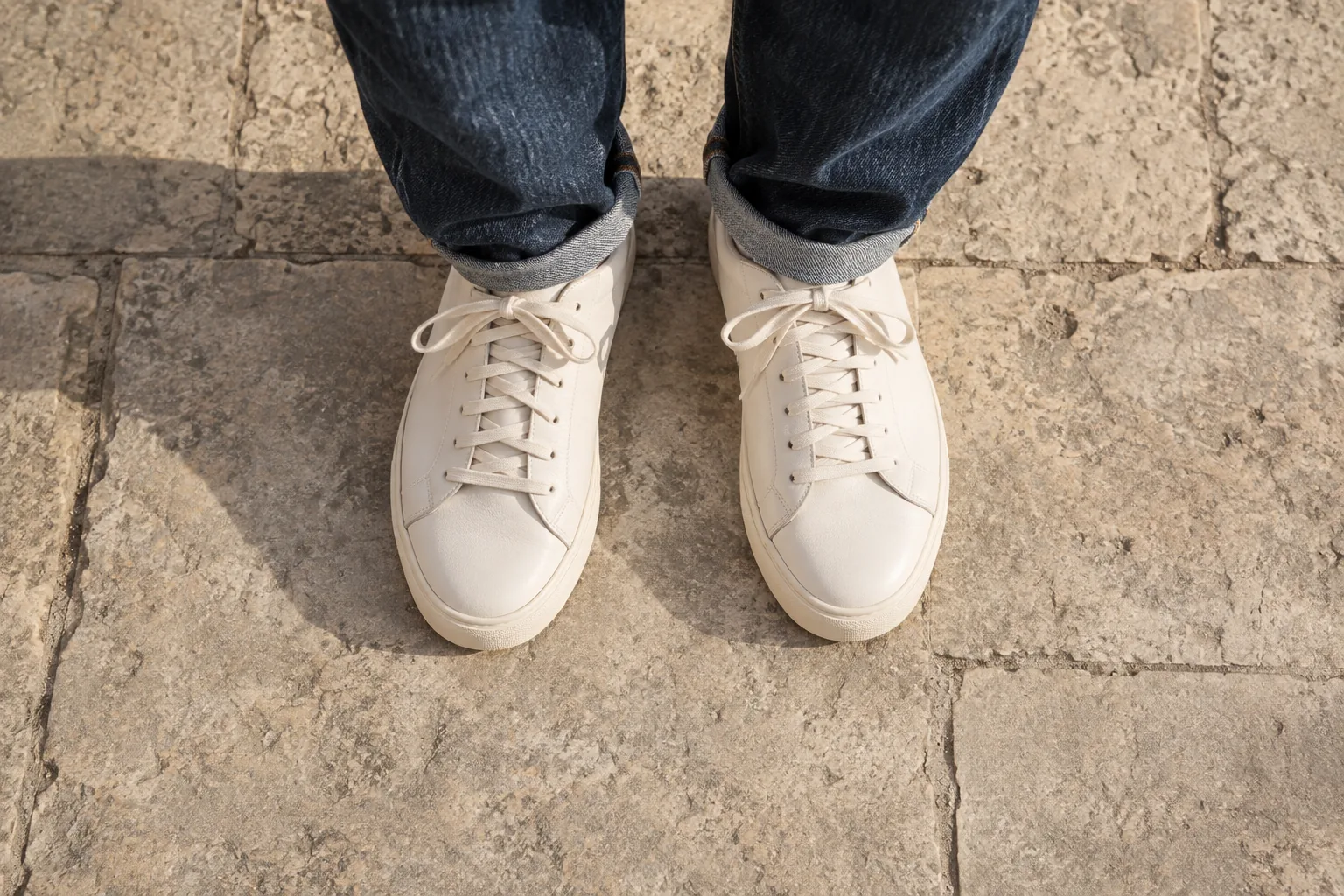 Rounded sneaker toe shapes seen from above, worn with relaxed denim on pale stone